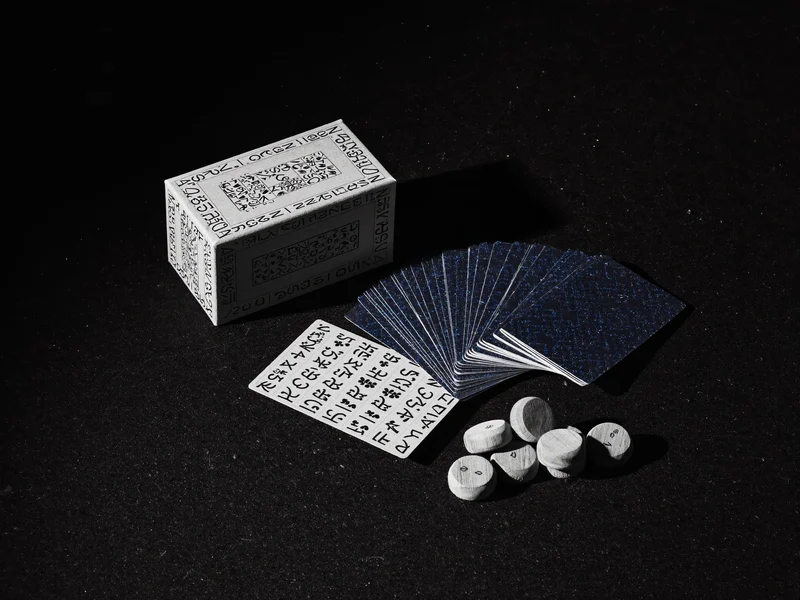 Gefächerte Spielkarten neben schlichter Kartenschachtel und Holzmarkern auf dunklem Filz
