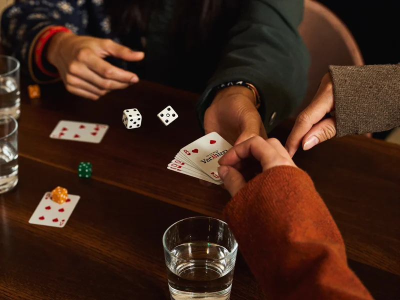 Hände über dem Tisch beim Spieleabend mit rollenden Würfeln und gehaltenen Karten